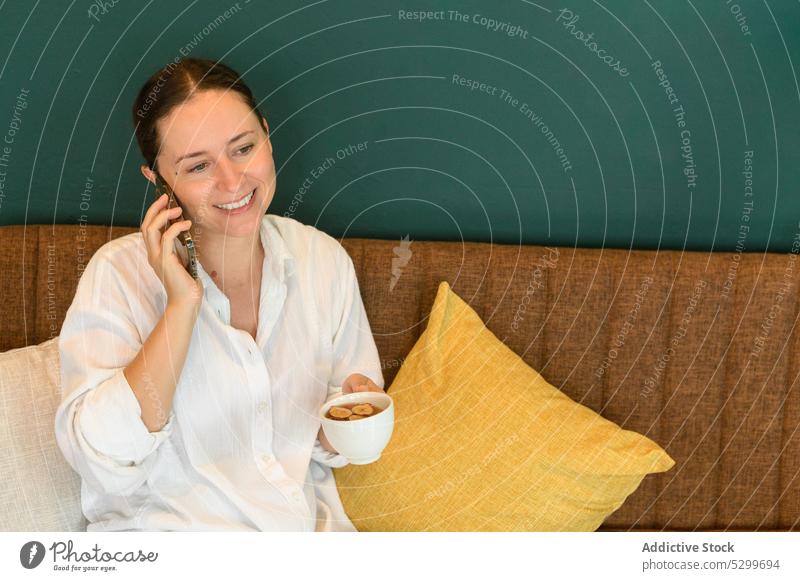 Lächelnde Frau spricht mit ihrem Smartphone und trinkt Tee in einem Café reden Cappuccino Kaffeepause benutzend trinken heiter Pause heiß Getränk Mobile Vietnam