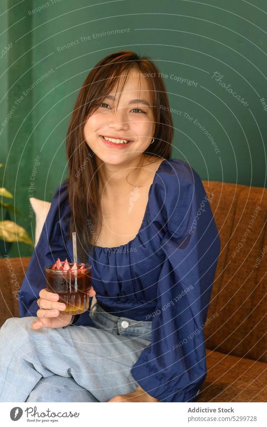 Fröhliche asiatische Frau mit Erfrischung in einem Cafe Lächeln Café Laptop trinken positiv Glück Kaffee heiter Getränk Stroh Glas Vietnam ethnisch froh Sofa