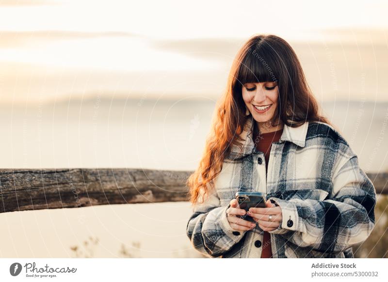 Positiv eingestellte Frau, die während einer Reise auf ihrem Smartphone surft Wald benutzend Browsen Lächeln heiter Nachricht Natur Glück Wochenende Mobile jung