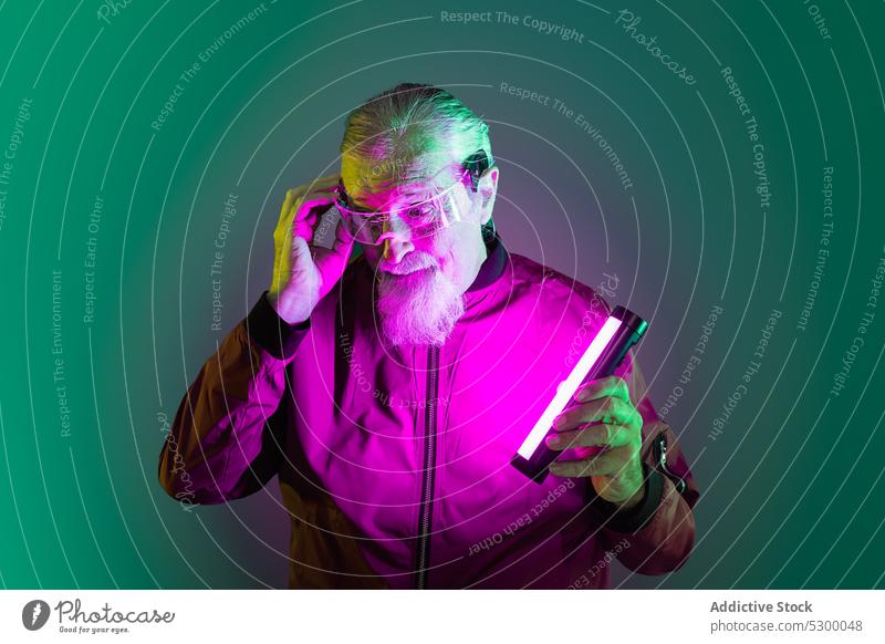 Verblüffter älterer Mann mit Neonlicht neonfarbig Hipster Überraschung erstaunt Tastkopf Vollbart Stil Brille Schock männlich lässig Senior Licht besinnlich