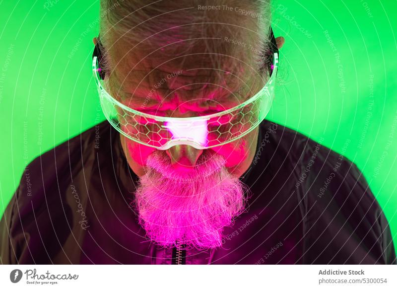 Ernster Mann mit Schutzbrille im Neonlicht neonfarbig Hipster leuchten Stil Farbe Vollbart ernst Brille behüten älter Senior maskulin männlich glühen stehen