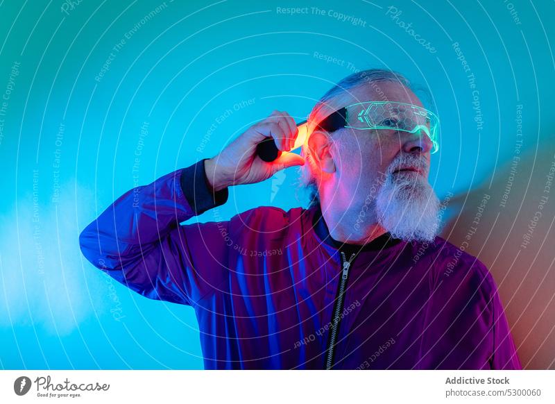Nachdenklicher älterer Mann mit Neonlampe Hipster neonfarbig Atelier selbstbewusst Vollbart ernst Stil graues Haar Brille leuchten männlich Senior Lampe