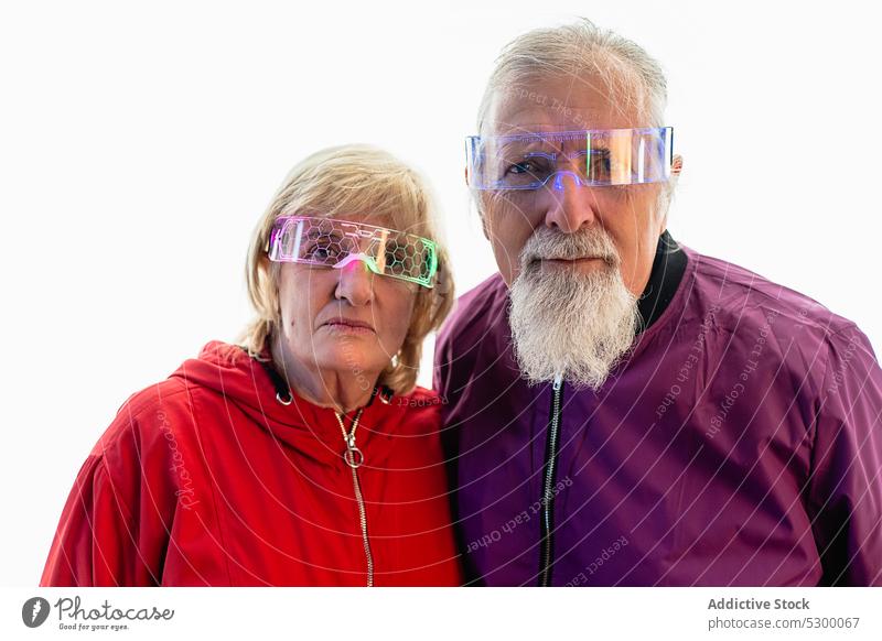 Älteres Paar steht in der Nähe einer weißen Wand und schaut in die Kamera ernst selbstbewusst besinnlich nachdenklich Partnerschaft Windstille hell Brille