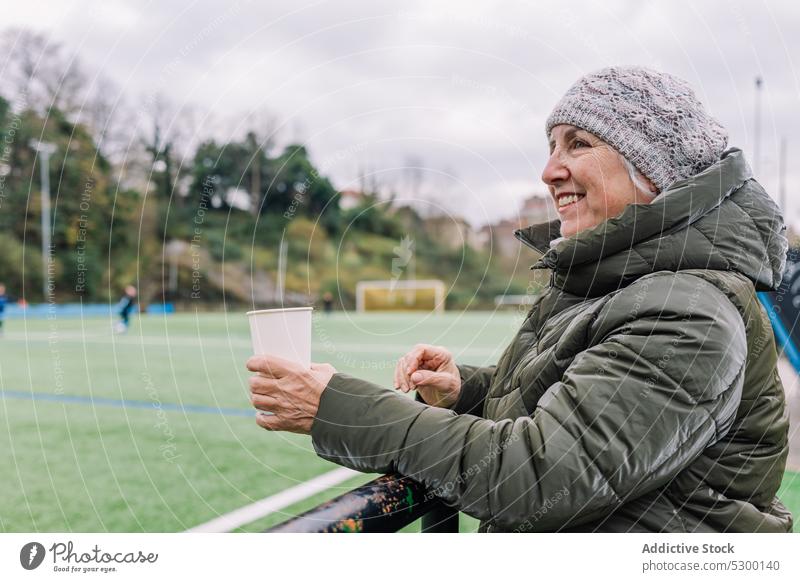 Fröhliche Seniorin mit Kaffee zum Mitnehmen Frau Imbissbude Fußball Streichholz Stadion Glück heiter trinken Lächeln Tasse positiv reif Spiel Sport genießen