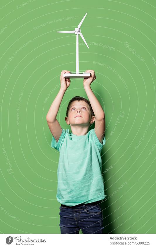 Lächelndes Kind mit Windrad-Attrappe über dem Kopf Junge Glück Overhead Kraft Windmühle Energie eolicisch Erzeuger Fokus lässig heiter Freude Kindheit positiv