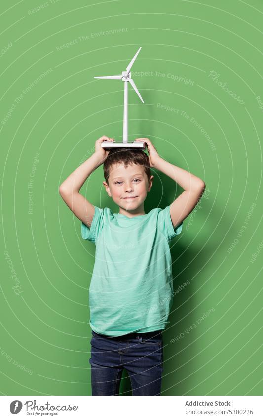Lächelndes Kind mit Windrad-Attrappe auf dem Kopf Junge Glück Kraft Windmühle Energie eolicisch Erzeuger lässig heiter Freude Kindheit positiv aufgeregt