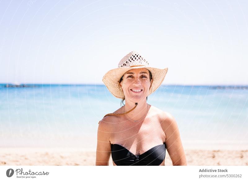 Lächelnde Frau mit Hut am Sandstrand stehend Strand MEER Sommer Ufer Stil Glück Urlaub heiter jung Freude froh Feiertag positiv Wasser Optimist reisen Resort