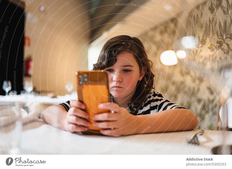 Konzentriertes Mädchen, das im Restaurant ein Video auf dem Smartphone anschaut zuschauen benutzend Konzentration online Café Apparatur Browsen Gerät Fokus Kind