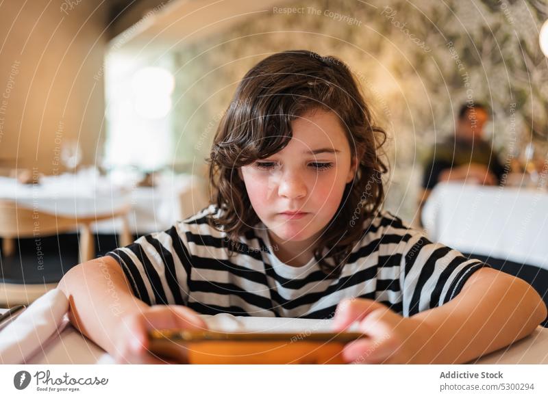 Konzentriertes Mädchen, das im Restaurant ein Video auf dem Smartphone anschaut zuschauen benutzend Konzentration online Café Apparatur Browsen Gerät Fokus Kind