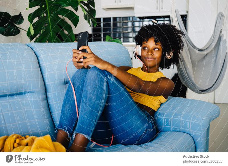 Zufriedene schwarze Frau macht Selfie auf der Couch zu Hause Smartphone Kopfhörer zuhören Freizeit online benutzend Browsen Internet heimwärts Musik
