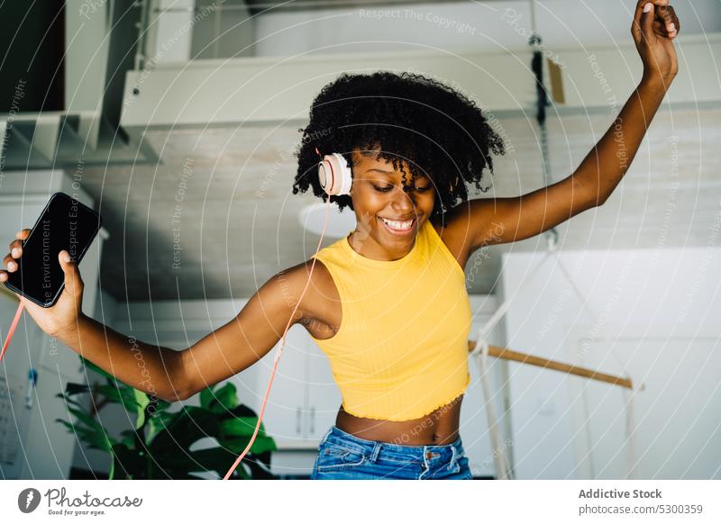 Fröhliche schwarze Frau tanzt auf dem Sofa Tanzen zuhören Musik heimwärts Kopfhörer Smartphone Glück benutzend Afroamerikaner jung ethnisch lässig krause Haare