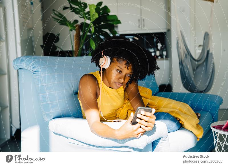 Zufriedene schwarze Frau macht Selfie auf der Couch zu Hause Smartphone Kopfhörer zuhören Freizeit online benutzend Browsen Internet heimwärts Musik