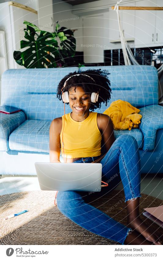 Glückliche schwarze Frau arbeitet am Laptop freiberuflich Arbeit Lächeln Kopfhörer froh Freude Browsen Tippen benutzend heimwärts Afroamerikaner jung lässig