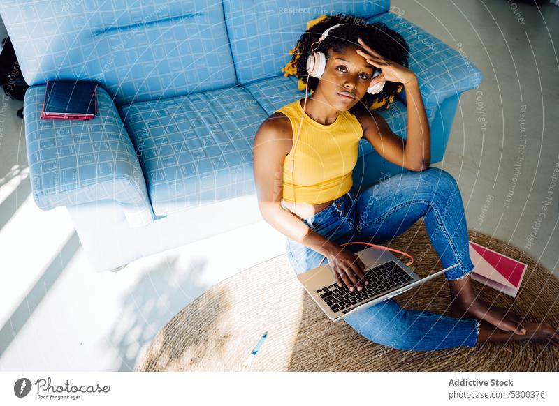 Nachdenkliche schwarze Frau arbeitet am Laptop freiberuflich Arbeit Kopfhörer Browsen Tippen nachdenklich benutzend heimwärts Afroamerikaner jung lässig
