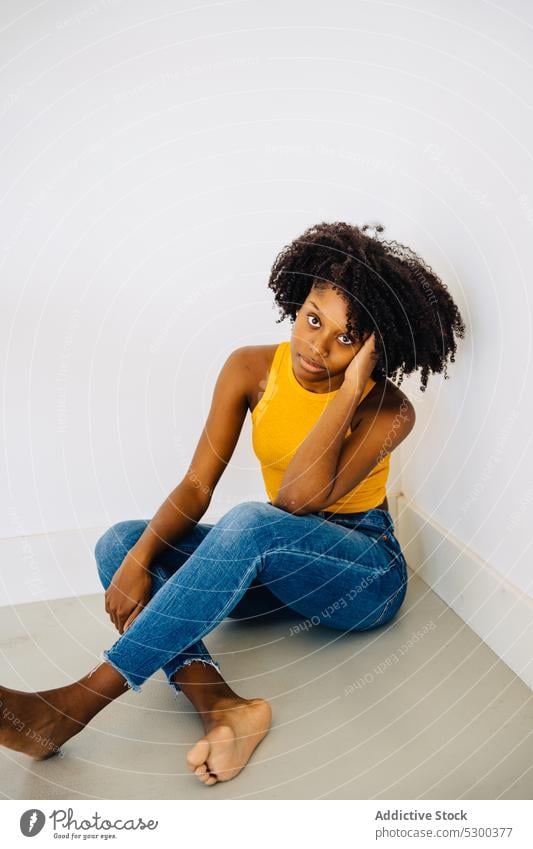 Ruhige schwarze Frau auf dem Boden sitzend nachdenklich Windstille besinnlich ernst Vorschein krause Haare Frisur Barfuß ruhig jung Afroamerikaner lässig Stil
