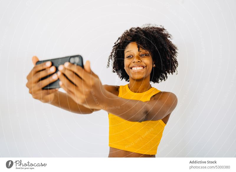 Fröhliche schwarze Frau macht Selfie Smartphone Selbstportrait benutzend Afro-Look Grimasse heiter Glück Afroamerikaner ethnisch Frisur Top gestikulieren jung