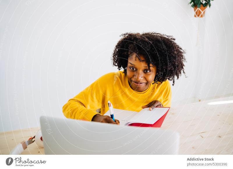 Zufriedene schwarze Frau, die in einen Notizblock schreibt zur Kenntnis nehmen Laptop Schüler Notebook lernen Bildung schreiben Hausaufgabe Prüfungsvorbereitung