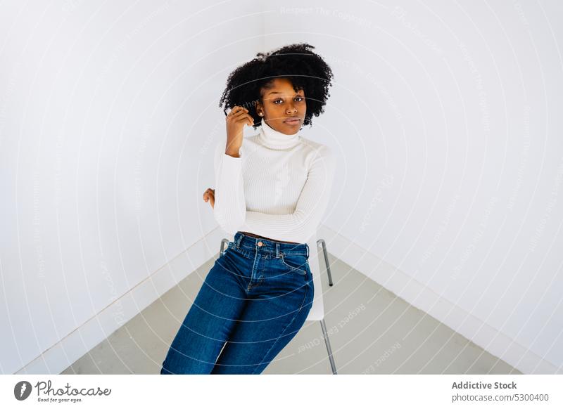 Trendy schwarze Frau sitzt auf einem Stuhl Mode Atelier Stil selbstbewusst Model Outfit ernst trendy Afroamerikaner schlank jung Vorschein Körperhaltung