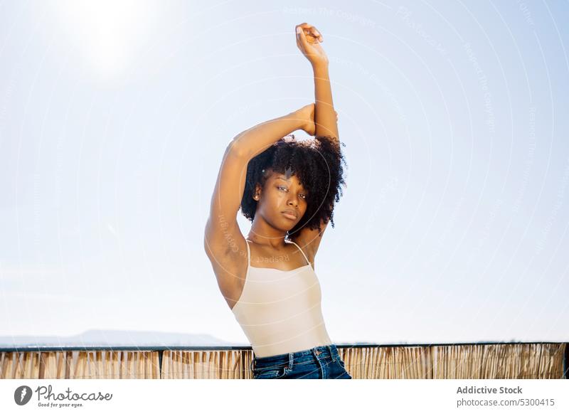 Schlanke schwarze Frau streckt Arme aus Dehnung Stil selbstbewusst lässig Balkon krause Haare Afro-Look ruhig jung Afroamerikaner Outfit trendy brünett