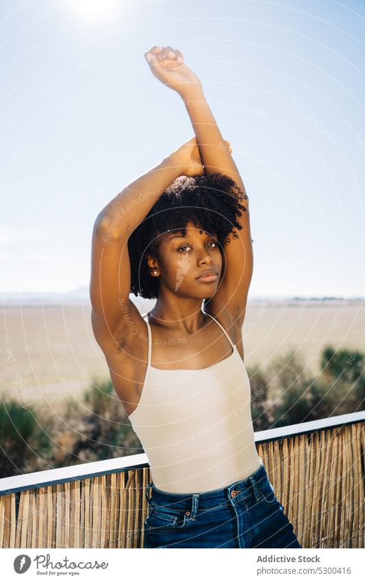 Schlanke schwarze Frau streckt Arme aus Dehnung Stil selbstbewusst lässig Balkon krause Haare Afro-Look ruhig jung Afroamerikaner Outfit trendy brünett
