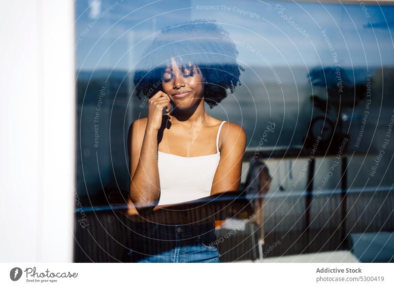 Trendige schwarze Frau mit geschlossenen Augen am Fenster Windstille Afro-Look besinnlich Lächeln Reflexion & Spiegelung Frisur heimwärts froh