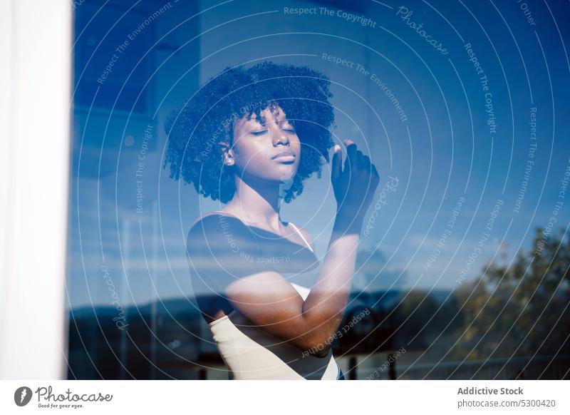 Trendige schwarze Frau mit geschlossenen Augen am Fenster Windstille ernst Afro-Look besinnlich Reflexion & Spiegelung Frisur heimwärts afroamerikanische Frau