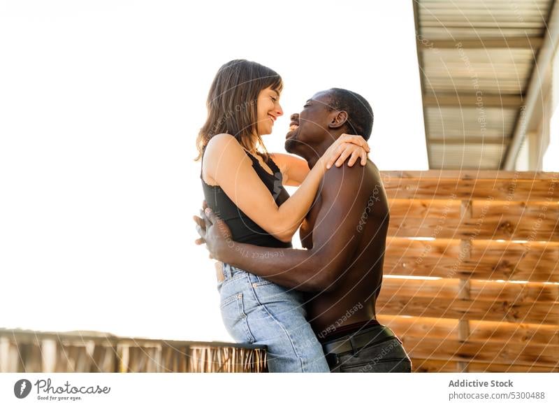 Positives multiethnisches Paar beim Kuscheln auf der Terrasse Lachen Umarmen Zusammensein heiter Balkon Liebe Umarmung Glück Partnerschaft Haus