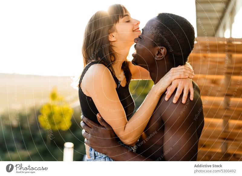 Positives multiethnisches Paar beim Kuscheln auf der Terrasse Lachen Umarmen Zusammensein heiter Balkon Liebe Umarmung Glück Partnerschaft Haus Kuss