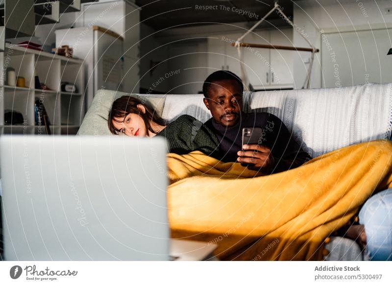 Ernster schwarzer Mann surft auf seinem Smartphone, während er mit seiner Freundin einen Film ansieht Paar Laptop zuschauen Wochenende Zeit verbringen ruhen