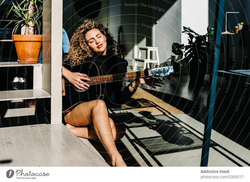 Konzentrierte Frau spielt Gitarre auf dem Boden spielen Musik Musiker Instrument Gitarrenspieler üben Fenster Hobby akustisch jung Melodie Talent Klang