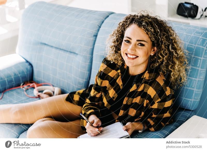 Lächelnde Frau schreibt Notizen in Zwischenablage zur Kenntnis nehmen schreiben zu Hause Sofa Wochenende Vorstellungskraft Gedanke komponieren positiv jung