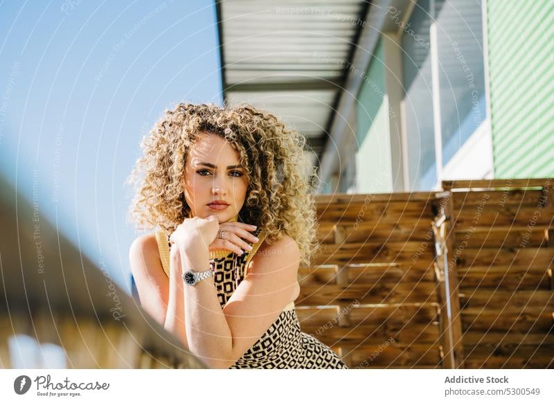 Attraktive lockige Frau lehnt sich an ein Holzgeländer Balkon anlehnen Reling Blauer Himmel Wolkenloser Himmel Sonnenlicht krause Haare Sommer Charme attraktiv