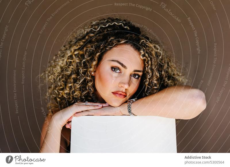 Junge attraktive Frau lehnt sich an einen weißen Würfel Model Studioaufnahme Porträt Make-up Vorschein anlehnen krause Haare Individualität jung emotionslos