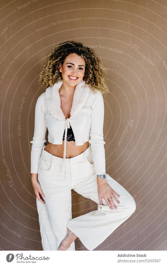 Lächelnde Frau in weißer Kleidung vor braunem Hintergrund Model Studioaufnahme sorgenfrei Vorschein hübsch krause Haare charismatisch Atelier