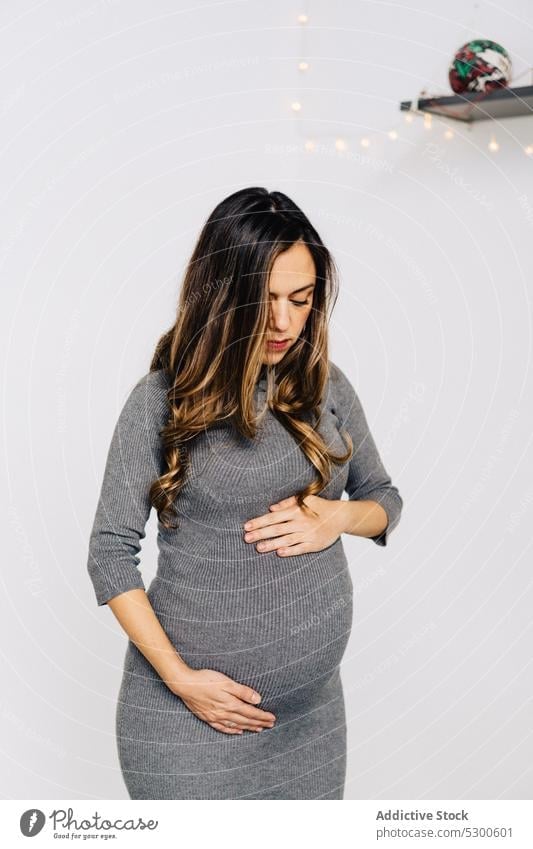 Glückliche schwangere Frau, die ihren Bauch berührt Bauch anfassen Girlande glühen warten führen Baby erwarten aufgeregt Lächeln jung Stil Kleid pränatal