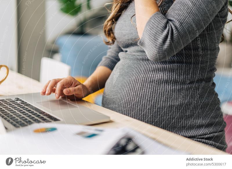 Anonyme, konzentrierte Frau, die an einem Laptop arbeitet und ihren schwangeren Bauch berührt benutzend online Projekt abgelegen Job Arbeit freiberuflich Fokus