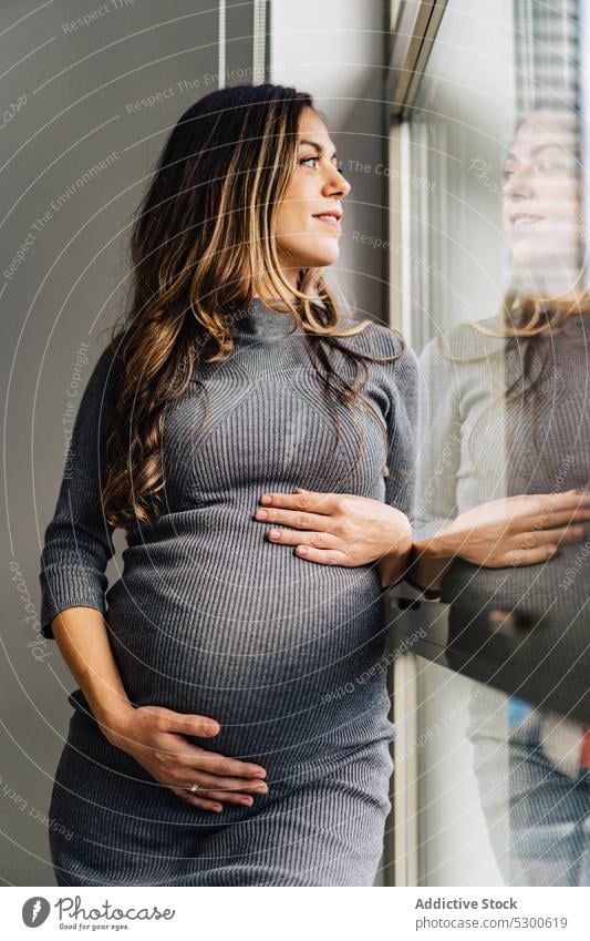 Schwangere Frau steht am Fenster und streichelt ihren Bauch schwanger Liebe Streicheln Bauch anfassen Mutterschaftsurlaub vorwegnehmen ruhig warten Lächeln jung