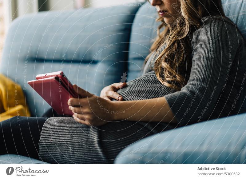 Anonyme schwangere Frau benutzt Tablette zuschauen Film Mutterschaftsurlaub Freizeit Sofa zu Hause Lächeln jung Anschluss kariert Drahtlos gewelltes Haar