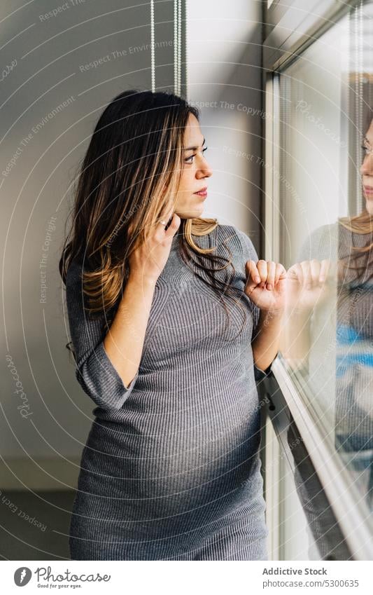 Lächelnde schwangere Frau, die mit einem Handy telefoniert benutzend Smartphone sprechen Fenster Telefonanruf Appartement Gespräch Kommunizieren positiv jung