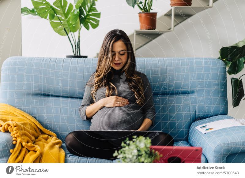 Lächelnde schwangere Frau sieht sich einen Film auf einem Tablet an zuschauen Tablette Mutterschaftsurlaub Freizeit Sofa zu Hause jung Anschluss kariert