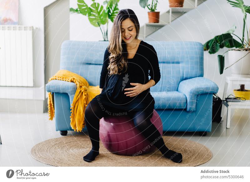 Fröhliche schwangere Frau, die zu Hause auf einem fitten Ball sitzt Training Übung Passform-Ball Wohlbefinden Bauch anfassen Mutterschaftsurlaub Freizeit
