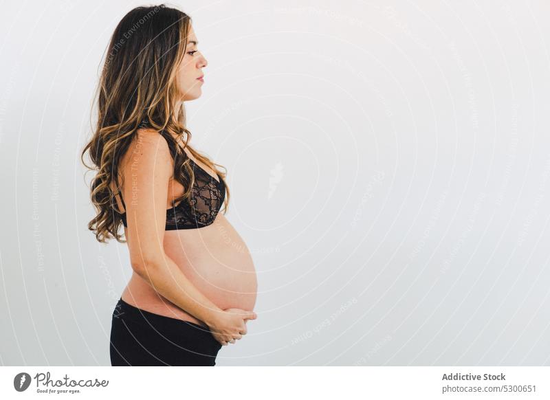 Junge Frau mit Baby vor weißem Hintergrund schwanger Studioaufnahme Mutterschaftsurlaub Pflege Liebe warten Streicheln Bauch anfassen Babybauch Unterwäsche jung