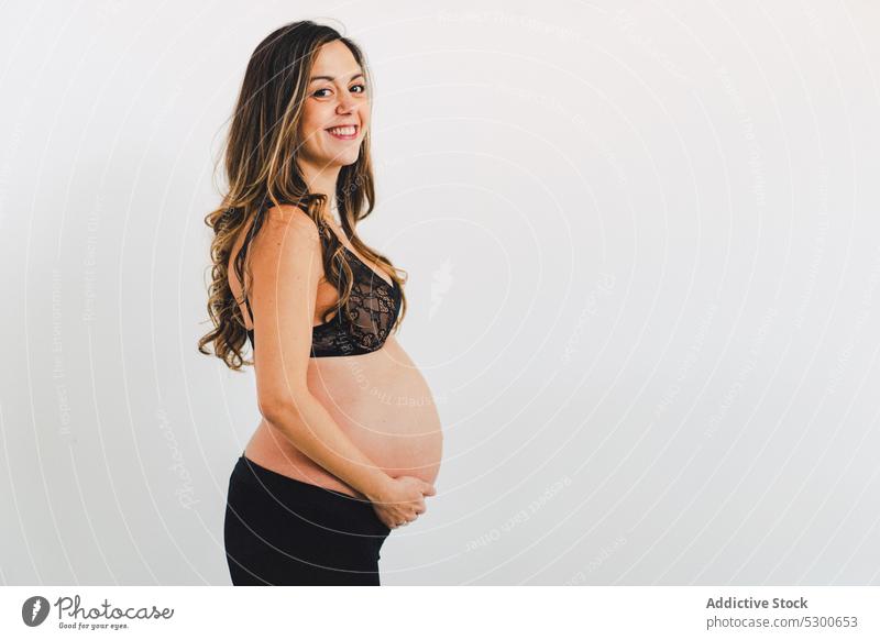 Junge lächelnde Frau mit Baby vor einem weißen Hintergrund schwanger Studioaufnahme Glück Mutterschaftsurlaub Pflege Lächeln Liebe warten froh Streicheln