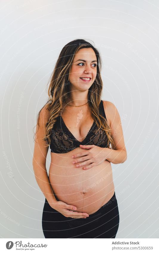 Junge lächelnde Frau mit Baby vor einem weißen Hintergrund schwanger Studioaufnahme Glück Mutterschaftsurlaub Pflege Lächeln Liebe warten froh Streicheln Freude