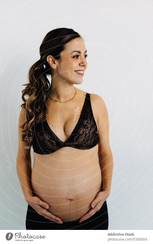 Junge lächelnde Frau mit Baby vor einem weißen Hintergrund schwanger Studioaufnahme Glück Mutterschaftsurlaub Pflege Lächeln Liebe warten froh Streicheln Freude
