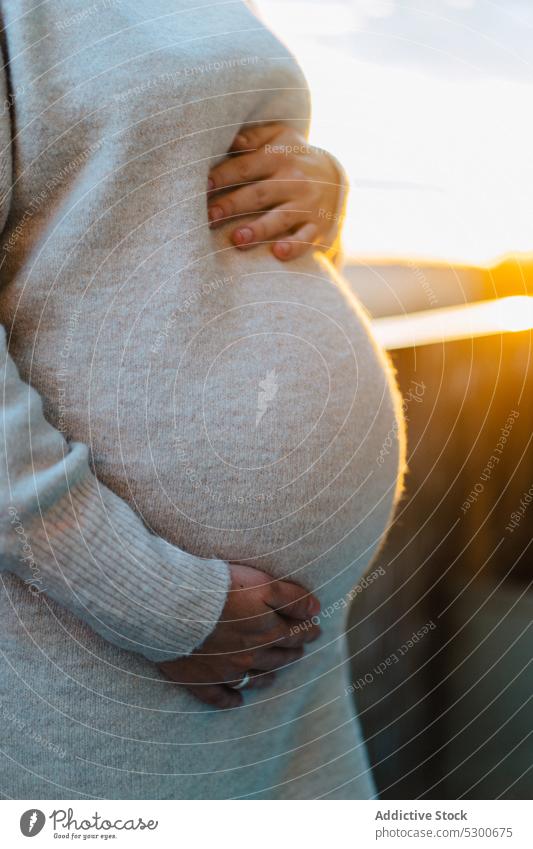 Anonyme schwangere Frau, die ihren Bauch auf der Terrasse umarmt ungeboren Baby Angebot Liebe Streicheln Bauch anfassen Sonnenlicht Sonnenuntergang jung