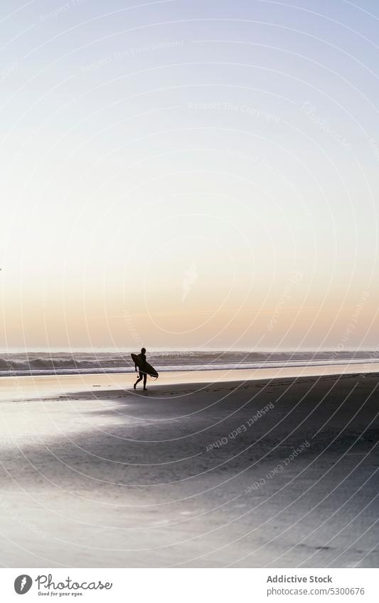 Silhouette einer nicht erkennbaren Person mit Surfbrett, die am Meer entlang läuft Strand MEER Sonnenuntergang Spaziergang Sand Abend winken Surfer Küste Ufer