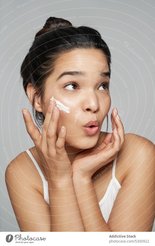 Zufriedene Frau beim Eincremen des Gesichts im Studio Sahne bewerben Hautpflege Feuchtigkeit Leckerbissen Kosmetik positiv Schönheit Schliere Kosmetologie
