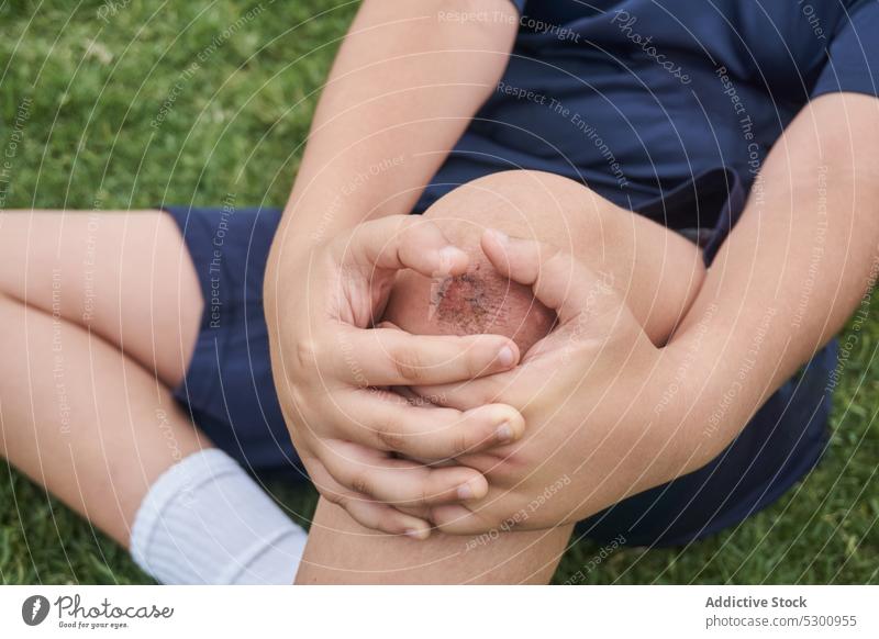 Junge sitzt nach Verletzung im Gras ruhen verletzen ertragen Schmerz Schmerzen Sportbekleidung wehtun Rasen Athlet Sitzen Problematik unglücklich Knie