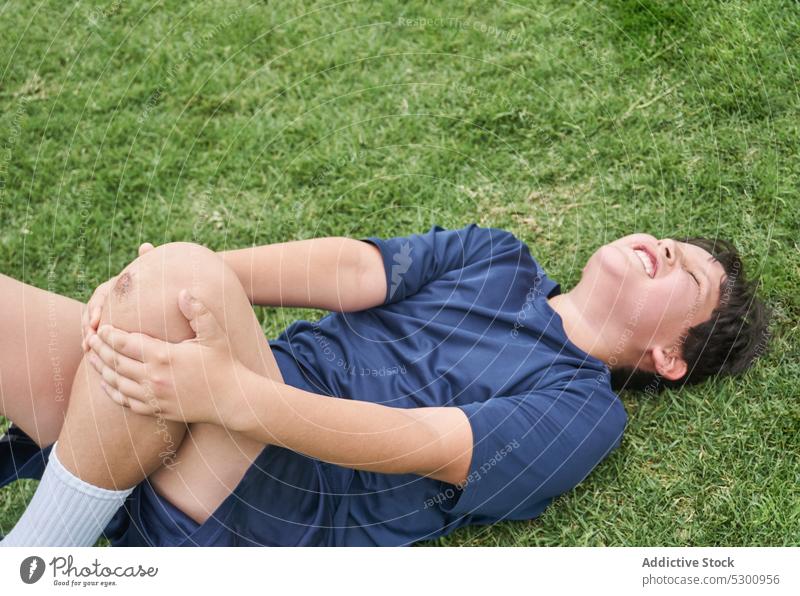 Verärgerter Junge liegt nach Verletzung im Gras müde ruhen verletzen ertragen Schmerz Schmerzen Sportbekleidung wehtun Rasen Athlet Lügen Augen geschlossen